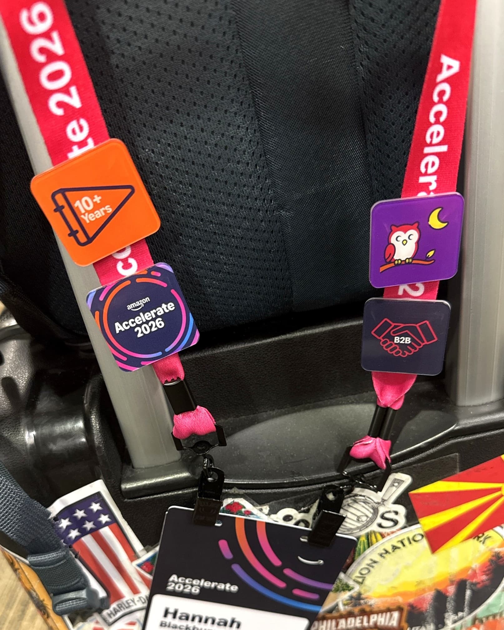Hannah's Amazon Accelerate 2026 lanyard clipped to a sticker-covered suitcase, with the badges she picked: 10+ Years, a night owl and B2B.