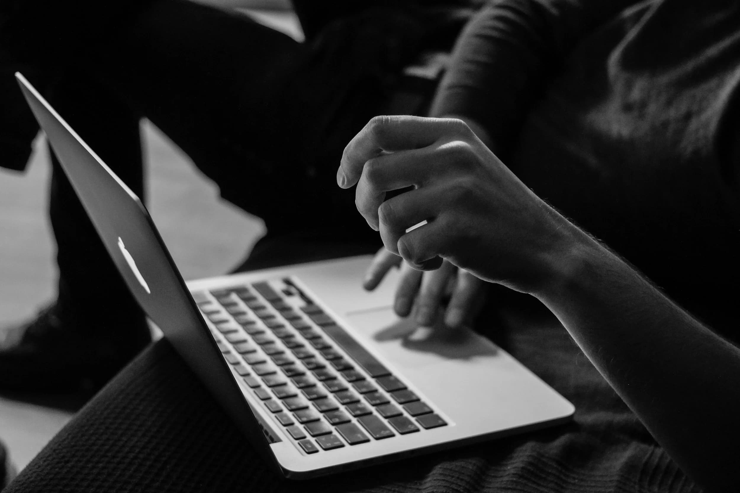 Black and white photograph of hands typing on a laptop.